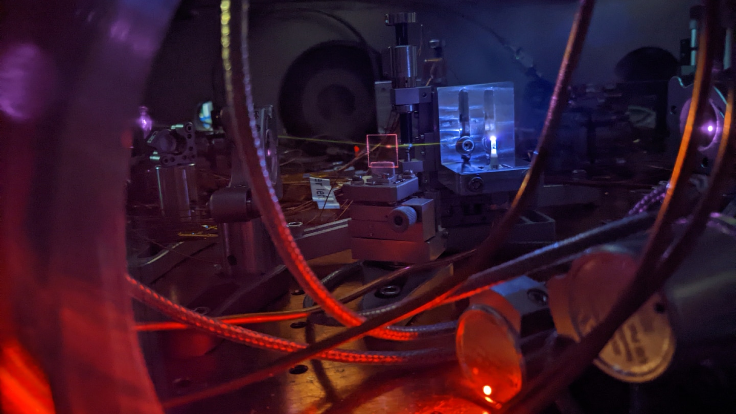 A photograph of scientific equipment, including a laser beam that illuminates gas inside a vacuum room.